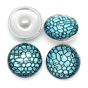 May include: Four circular snap buttons featuring a metallic silver base and a domed top with a vibrant turquoise blue and black honeycomb or reptilian scale pattern. The buttons have a smooth, glossy finish and a standard metal snap fastener mechanism.