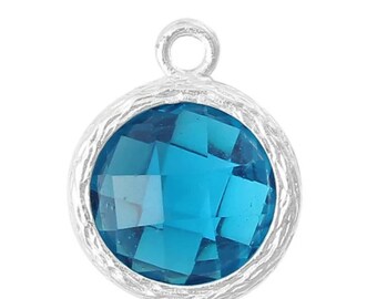 May include: A silver charm with a round, textured bezel and a blue faceted gemstone.