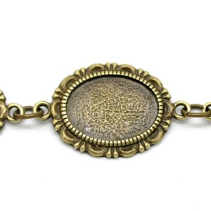 May include: A close-up of a gold-toned metal chain with oval-shaped frames. The frames have a textured surface and are connected by small metal links.