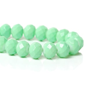 May include: Close-up of a string of light green faceted beads. The beads are round with multiple flat surfaces, creating a sparkling effect. The beads are strung together, suitable for jewellery making or crafting projects.