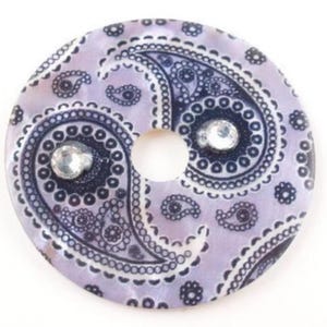 May include: A round, purple and white paisley patterned disc with two clear rhinestones. The disc has a hole in the center.