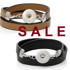 Könnte beinhalten: Zwei Leder-Wickelarmbänder mit silbernen Druckknöpfen und einer silbernen Kette. Das Armband links ist braun und das Armband rechts ist schwarz. Das Wort "VERKAUF" ist in roten Buchstaben unter den Armbändern gedruckt.