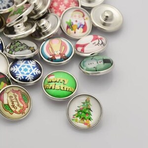 May include: Assortment of Christmas themed snap buttons with various designs, including a snowman, a Christmas tree, a reindeer, and the words "Merry Christmas".