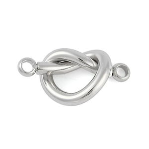 May include: A polished silver-toned knot clasp, featuring a heart-shaped design. The clasp has two circular loops on either end for attachment. The metal has a smooth, reflective surface, and the overall design is simple and elegant.