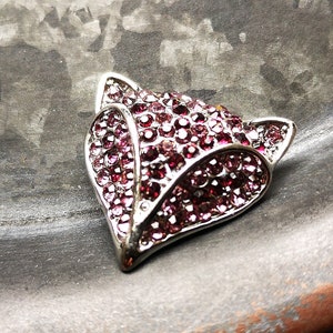 May include: A fox-shaped brooch crafted from silver-toned metal, featuring a dense pav&eacute; setting of small, round, deep pink and magenta crystals that cover the entire surface of the fox head, including the pointed ears and the snout.