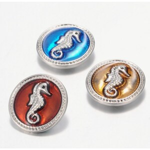 May include: Three circular buttons with silver-toned metal rims and textured edges. Each button features a raised, silver-coloured seahorse relief centred on a smooth, glossy inlay. The inlays are coloured in vibrant blue, deep red, and amber.