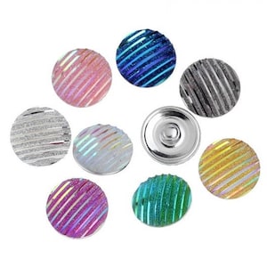 Könnte beinhalten: Eine Sammlung dekorativer Druckknöpfe in verschiedenen Farben, darunter Rosa, Blau, Silber und Grün. Jeder Knopf hat eine runde Form mit einem strukturierten, diagonal gestreiften Muster und einem glänzenden, metallischen Finish.