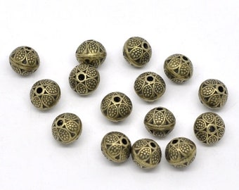 May include: A collection of antique brass-colored metal beads. Each bead is spherical, featuring a detailed floral pattern and small circular openings. The beads are scattered on a white surface, showcasing their intricate design.