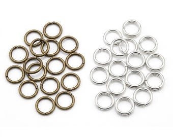 May include: A collection of metal jump rings arranged in two distinct groups. The left group consists of antique bronze-colored circular rings, while the right group features bright silver-colored circular rings. Each ring has a small split opening.
