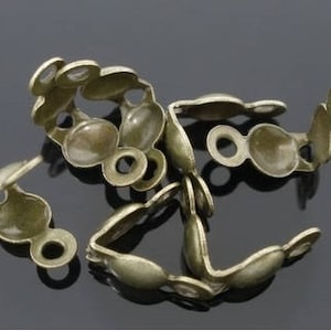May include: Several antique brass-colored crimp bead end caps. Each cap has a rounded, oval shape with a small loop on each end. These jewelry findings are used to secure the ends of beaded strands.