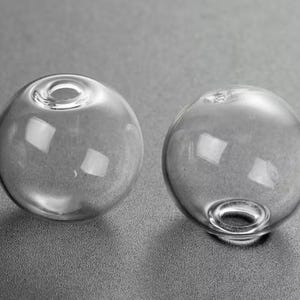 May include: Two clear glass spheres with a small hole at the top. The spheres are smooth and round.