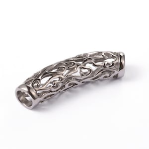 May include: A silver-coloured, cylindrical bead with an openwork design. The bead has a curved shape and features a repeating pattern of swirling, flame-like shapes. The ends of the bead are smooth and rounded.