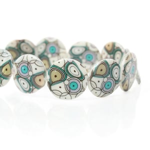 May include: A strand of white oval beads with a teal, brown, and white abstract pattern.
