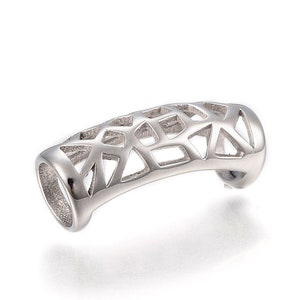 May include: A silver-coloured ring with a geometric pattern. The ring has a tubular shape with an open, angular design. The metal appears polished, reflecting light. The ring is curved and has a smooth, rounded edge on each end.