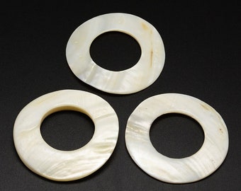 May include: Three white mother of pearl rings with a smooth, polished finish. The rings are approximately 2 inches in diameter and have a hole in the center.