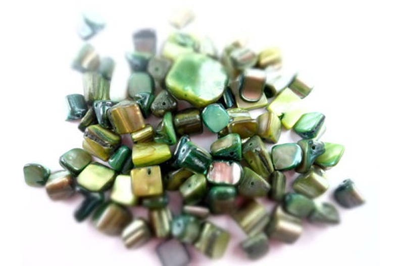 May include: A collection of green and gold iridescent shell beads. The beads are various shapes and sizes, with some being square, rectangular, and triangular.