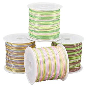 May include: A collection of colorful spools of cord. The cords are wound on white plastic spools. The cords are in various colors, including pink, yellow, green, and brown. The cords are likely used for crafting or jewelry making.
