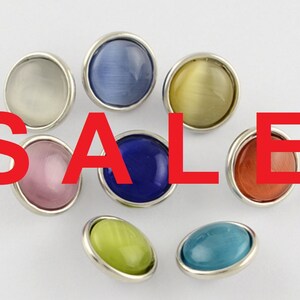 Può includere: Assortimento di otto bottoni decorativi rotondi, a fondo piatto, con un bordo in metallo argentato. I bottoni sono di vari colori, tra cui blu, verde, rosa, giallo e rosso.