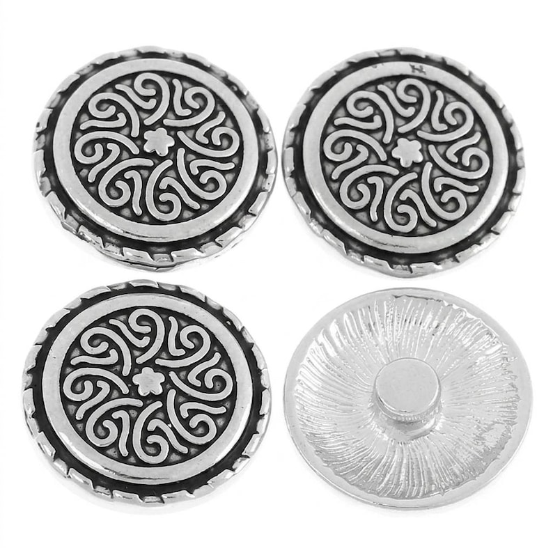 May include: Four round silver-toned metal buttons. Three buttons display a raised, intricate swirling pattern with a small flower at the centre and a rope-textured border. One button is shown from the back, revealing a smooth, flat circular attachment.