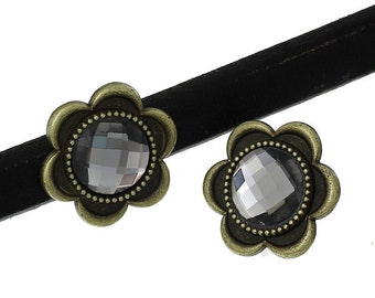 May include: A black choker necklace with two flower-shaped embellishments. Each flower has a faceted gray gem center surrounded by a bronze-colored metal frame. The choker is made of a thin, black material.