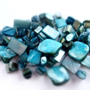 May include: A collection of blue and green iridescent glass beads, some are rectangular and some are irregular shapes.