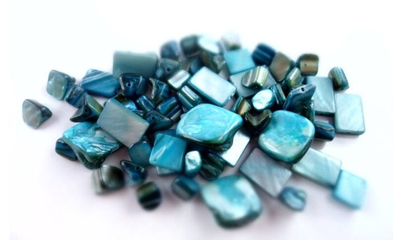 May include: A collection of blue and green iridescent glass beads, some are rectangular and some are irregular shapes.