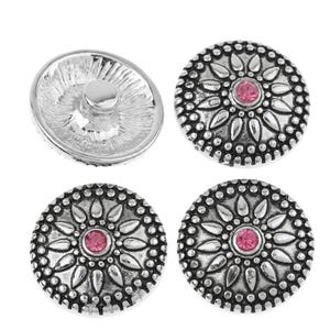 Könnte beinhalten: Vier kreisförmige Metalldruckknöpfe mit silberfarbenem Finish. Drei Knöpfe zeigen ein erhabenes Blumenmuster mit einem zentralen rosa Strassstein. Ein Knopf ist von der Rückseite abgebildet und zeigt den glatten Metallverschlussmechanismus.