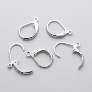 May include: Four silver-toned metal earring findings with lever-back closures. Each piece features a circular loop at the top for attaching jewelry components and a hinged mechanism that snaps securely into place to form a closed hoop shape.