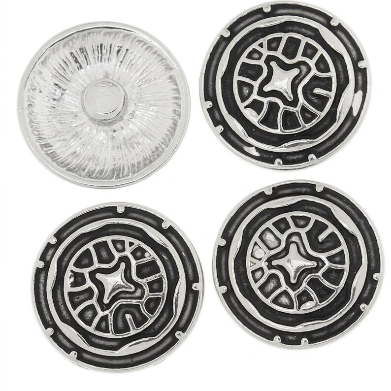 May include: Four circular buttons arranged in a square formation. Three buttons feature a black and silver metallic finish with a raised, intricate geometric pattern. One button is silver with a textured, radial sunburst design on its surface.