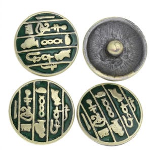 May include: Four round metal buttons featuring a dark green enamel inlay with raised gold-toned Egyptian-style hieroglyphic symbols. Three buttons show the front design, while one button is flipped to reveal the metallic back with a central shank.