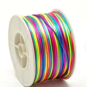 May include: A spool of colorful cord, featuring a vibrant array of rainbow colors. The cord is tightly wound on a white plastic spool. The colors include red, orange, yellow, green, blue, and purple.
