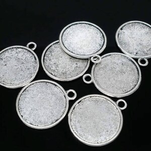 May include: A collection of silver-coloured, round pendant trays with a textured surface. Each tray has a small loop for attaching a chain or other embellishments. The trays are arranged on a black background.