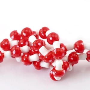 May include: A string of red and white glass beads shaped like mushrooms. The beads are strung together to create a necklace or bracelet.