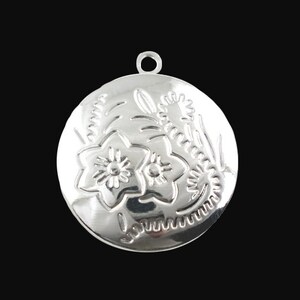 May include: Silver pendant featuring a floral design. The pendant is round and has a detailed floral pattern with two flowers and leaves.