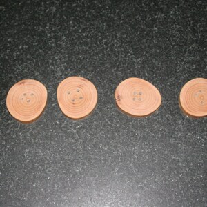 May include: Four round wooden coasters with a natural wood finish and a ring of holes around the centre.
