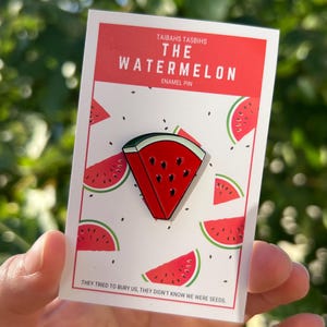 Puede incluir: Un pin de esmalte rojo y verde con forma de rebanada de sandía con semillas negras. El pin está en una tarjeta blanca con fondo rojo y el texto "TAIBAHS TASBIHS THE WATERMELON ENAMEL PIN THEY TRIED TO BURY US, THEY DIDN'T KNOW WE WERE SEEDS."