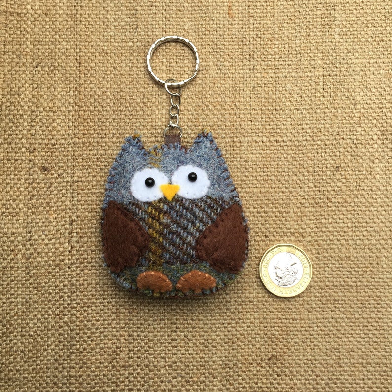 May include: A blue and brown felt owl keychain with yellow eyes and a brown beak. The owl is hanging from a silver key ring.
