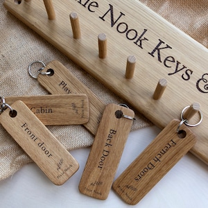 May include: Wooden key hooks with engraved labels for "Play", "Cabin", "Front door", "Back Door", and "French Doors". The hooks are mounted on a wooden board with the text "Pixie Nook Keys &" engraved on it.