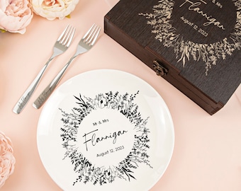 May include: A white ceramic plate with a black floral wreath design and the text "Mr. & Mrs. Flannigan August 12, 2023". A wooden box with a similar design and text is also shown.