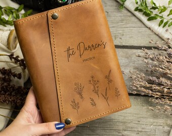 May include: A brown leather photo album with the text "The Darrens' Photos" engraved on the front. The album is decorated with a floral design.