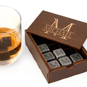 May include: A wooden box with a personalized engraved name "MICHAEL" on the lid. The box contains nine gray stone whiskey chilling cubes, each engraved with the letter "M".