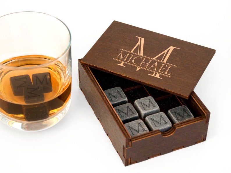May include: A wooden box with a personalized engraved name "MICHAEL" on the lid. The box contains nine gray stone whiskey chilling cubes, each engraved with the letter "M".
