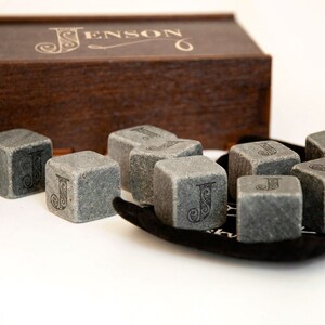 May include: A set of gray stone whiskey chilling cubes with the letter "J" engraved on each cube. The cubes are in a black velvet pouch and come in a wooden box with the name "Jenson" engraved on the top.