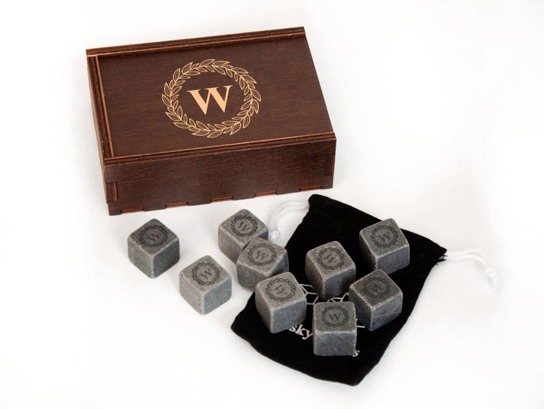 May include: A set of eight gray whiskey stones in a black velvet bag with a wooden box. The stones are engraved with a wreath and the letter "W".