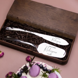 May include: A wooden box with a silver cake knife and server set. The knives are engraved with "MR & MRS Rodriguez" and the date "11.22.2023".