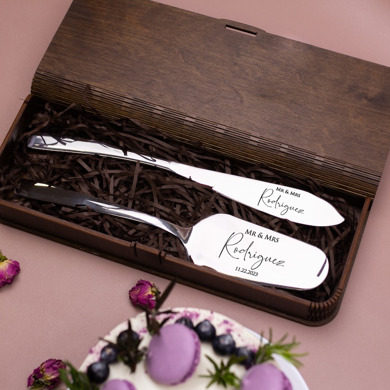 May include: A wooden box with a silver cake knife and server set. The knives are engraved with "MR & MRS Rodriguez" and the date "11.22.2023".