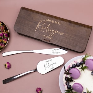 May include: A wooden box engraved with "MR & MRS Rodriguez 11.22.2023" and a set of two silver cake servers with the same engraving.