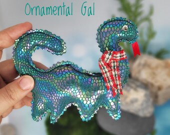 May include: A green, iridescent, fabric dragon with a red and white plaid scarf. The dragon is a handmade ornament.