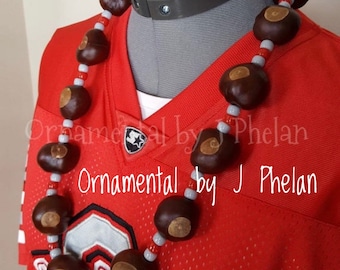 May include: A brown and gray buckeye necklace with red beads. The necklace is on a red jersey with a white "O" logo. The text "Ornamental by J Phelan" is visible on the jersey.