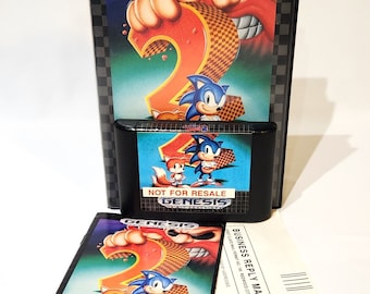 May include: A Sega Genesis game cartridge for Sonic the Hedgehog 2. The box art features a red and orange number 2 with a cartoon character's fist breaking through it. The cartridge is black with a blue label that says "Not for Resale" and "Genesis". The instruction manual is also included and features a cartoon image of Sonic and Tails.